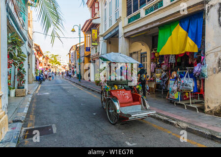 A local rickshaw (tuk tuk) driver in a colourful street scene in George Town, Penang Island, Malaysia, Southeast Asia, Asia Stock Photo