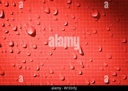 Large drops of water on a red textile with a waterproof effect. Water-repellent impregnation. Texture drops on the fabric. Stock Photo