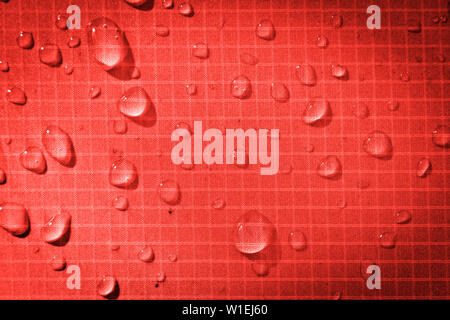Large drops of water on a red textile with a waterproof effect. Water-repellent impregnation. Texture drops on the fabric. Stock Photo