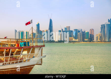 Close up of traditional wooden dhow with Qatari flag in Doha Bay in foreground and skyscraper towers of West Bay skyline in background, Doha, Qatar Stock Photo