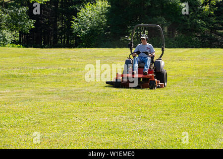 A male worker mowing a lawn with a commercial lawn mower in Speculator, NY USA Stock Photo