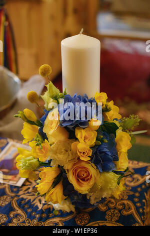 Baptismal candle decorated with a yellow spring flowers bouquet in preparation for the baptism, first of seven Sacraments in the Orthodox Church Stock Photo