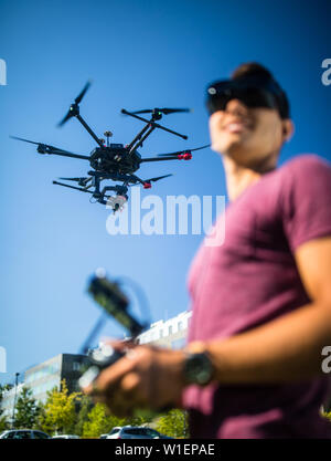 Handsome young man flying a drone outdoors using a VR/augmented reality glasses to operate the device, to see in real time the video feed from the dro Stock Photo