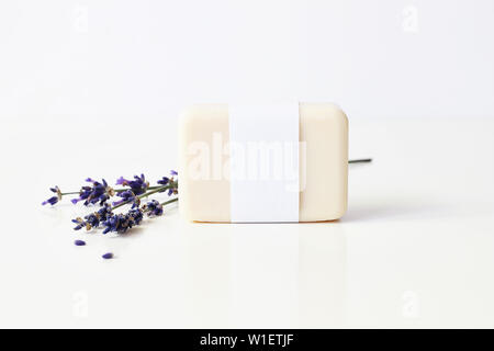 Closeup of hand made herbal soap bar in blank paper label package and bunch of lavender flowers on white table backround. Spa concept. Skin product Stock Photo