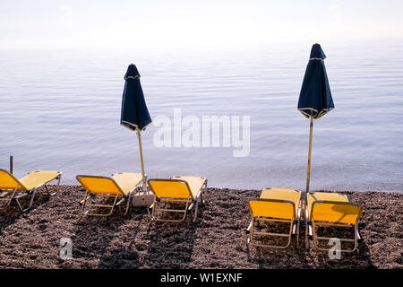Early morning on sandy beach without people with empty chaise lounges, sun beds, sunshades, summer umbrella parasol, deck chairs, table, loungers.