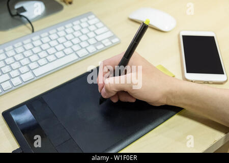 Hand using graphic tablet with smartphone on desk at workplace Stock Photo