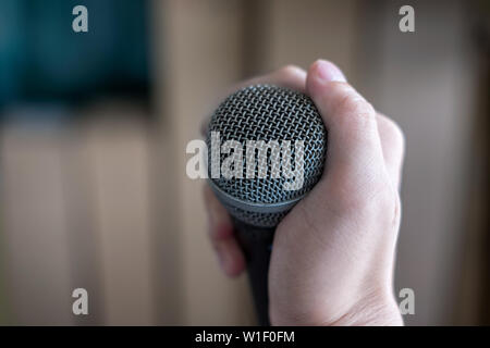 Hand holding a microphone on blurred background Stock Photo