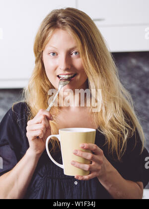Photo of a beautiful blond holding a large coffee in her kitchen. Stock Photo