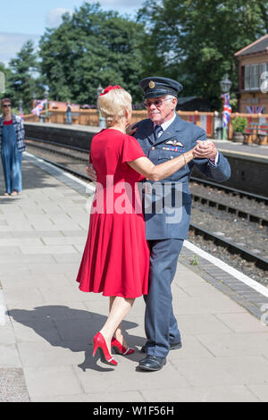 Kidderminster, UK. 29th June, 2019. Severn Valley Railways 'Step back to the 1940s' gets off to a fabulous start this summer weekend with costumed re-enactors playing their part in providing an authentic recreation of wartime Britain. A smartly-dressed couple in 1940's fashion are dancing together on the platform of a vintage railway station in the morning sunshine. Credit: Lee Hudson Stock Photo