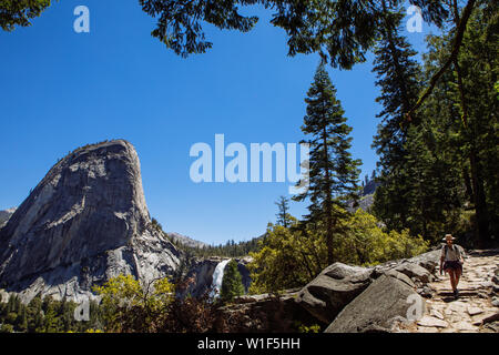 Tourist woman hiking through John Muir Trail with Nevada Fall and Liberty Cap, in summer with clear blue sky, Yosemite National Park, California, USA Stock Photo