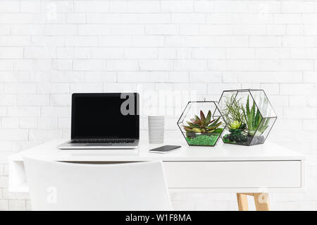 Desk with laptop and house plants at white brick wall background. Modern coworking place concept Stock Photo