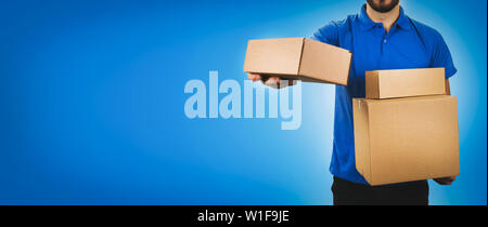 delivery service man holding cardboard boxes on blue background copy space Stock Photo