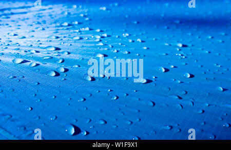Large drops of water on a blue textile with a waterproof effect. Water-repellent impregnation. Texture drops on the fabric. Selective focus Stock Photo