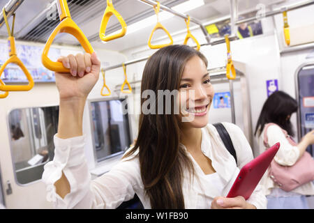 Subway commuter woman on Japanese public transport in Tokyo, Japan. Tourist using Japan's capital city metro system to commute. Portrait of happy asian lady holding handhold inside the wagon. Stock Photo