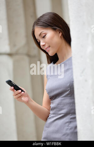 Urban smart casual businesswoman using app on smartphone. Young Asian Caucasian adult woman touching smart phone using 3g 4g app to read online or sms texting. Stock Photo