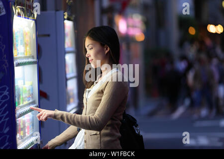Japan vending machines - Tokyo woman buying drinks. Japanese student or female tourist choosing a snack or drink at vending machine at night in famous Harajuku district in Shibuya, Tokyo, Japan. Stock Photo