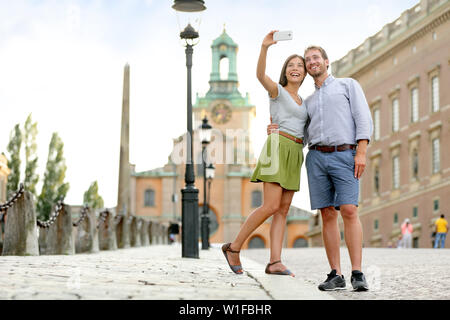 Selfie couple taking pictures at Stockholm cathedral and royal palace in Gamla Stan (Old Town) in the capital of Sweden. Tourists people taking travel photos with smartphone on summer holidays. Stock Photo