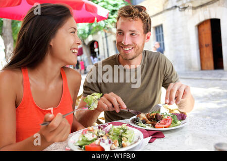 Restaurant tourists couple eating at outdoor cafe. Summer travel people eating healthy food together at lunch during holidays in Mallorca, Spain. Asian Caucasian multiracial young adults. Stock Photo