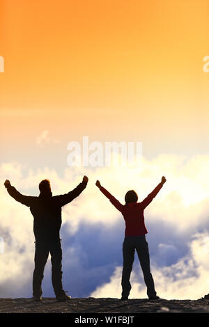 Success, life achievement, goal accomplishment concept with hiking people cheering and celebrating of joy with arms raised outstretched up in the sky outside on mountain summit. Stock Photo