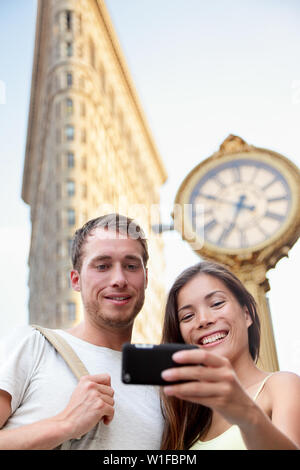 Travel couple taking selfie in New York City NYC, USA. Tourists holding smartphone to photograph self-portrait in front of famous Flatiron building downtown in summer. Stock Photo