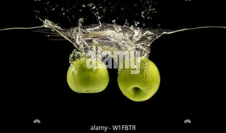 Two green apples sinking into water with air bubbles Stock Photo