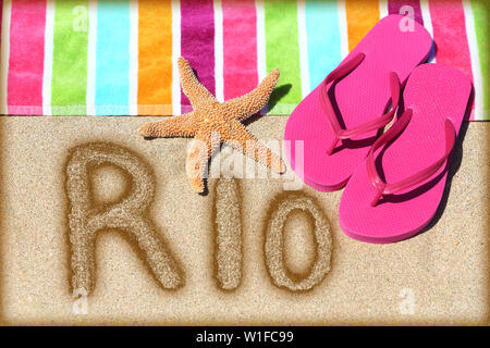 Rio beach concept. Overhead view ot the word RIO written on golden sand with a starfish, pink flip flops and towel conceptual of a summer vacation and travel in Rio de Janiero, Brazil Stock Photo