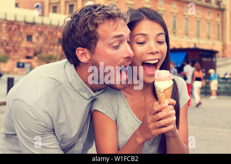 Funny playful young couple eating ice cream. Goofy portrait of boyfriend teasing girlfriend biting off a cold dessert in city summer, Stockholm, Sweden, Europe. Stock Photo