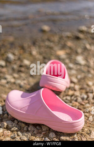 Pair of pink plastic clogs on shoreline beach in the summer Stock Photo