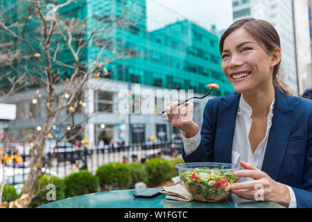 Business woman eating salad on lunch break in City Park living healthy lifestyle. Happy smiling multiracial young businesswoman, Bryant Park, Manhattan, New York City, USA Stock Photo