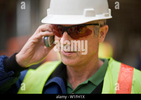 Mature adult male construction worker using a cellphone on a building site. Stock Photo