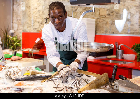 Positive seller in apron standing near counter offering fresh fish