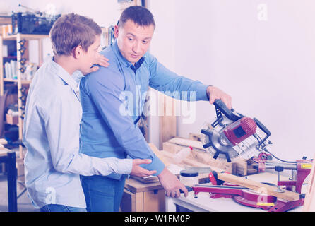 Positive glad guy and boy  restoring old wooden furniture with belt sander in workshop Stock Photo