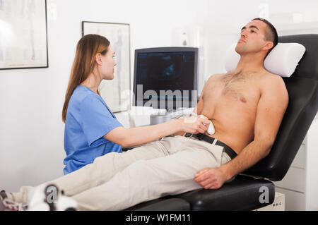 Female technician diagnosing male patient using modern ultrasound scanner in private clinic Stock Photo