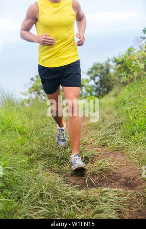 Fitness male runner jogging in running shoes outdoors in green grass trail path. Athlete man cardio workout in nature. Lower body crop for feet, legs, knees health problem pain, sportswear concept. Stock Photo