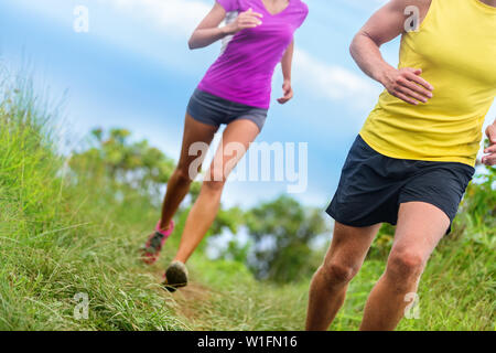 Fitness athletes trail running - athletic legs closeup lower body crop of man and woman working out. Sports people jogging in fast motion marathon race training on a nature path in shorts activewear. Stock Photo