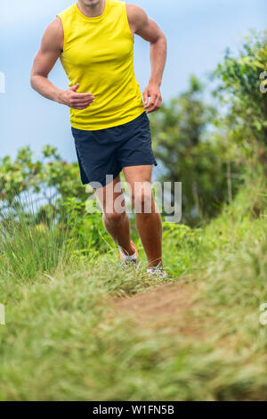 Man athlete running outside on a fitness trail run. Male runner jogging in sports shoes on grass path working out cardio in nature. Lower body crop for feet, legs, knees health pain challenge concept. Stock Photo