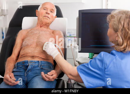 Diligent pleasant female technician diagnosing male patient using modern ultrasound scanner in private clinic Stock Photo