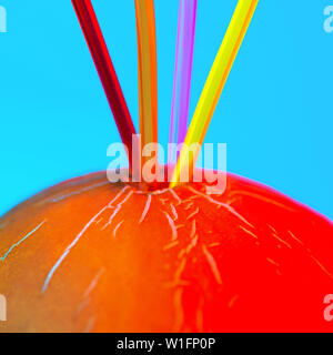 bright colored cocktail tubes stuck in a melon on a blue background Stock Photo