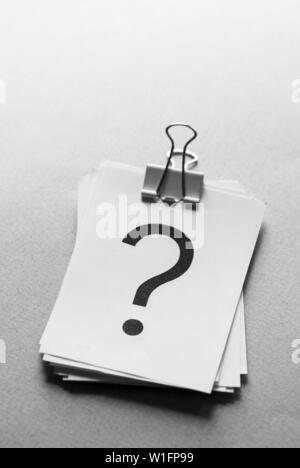 Stack of white cards printed with question marks held together with a metal paper clip over a grey background Stock Photo