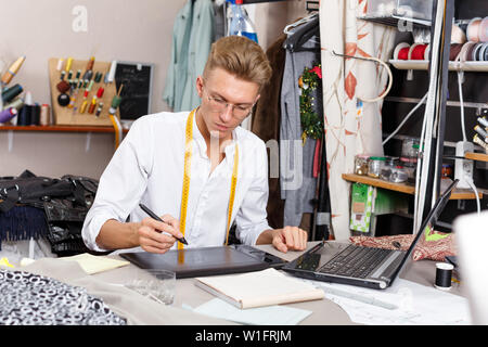 Professional male tailor at work – creating pattern using laptop and graphics tablet at his workplace Stock Photo