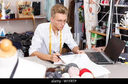 Professional male tailor at work – creating pattern using laptop and graphics tablet at his workplace Stock Photo