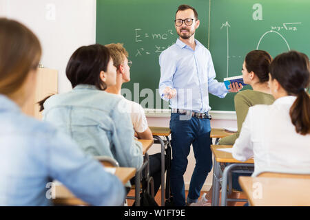 Young male teacher is giving interesting lecture for students during lesson in the classroom Stock Photo