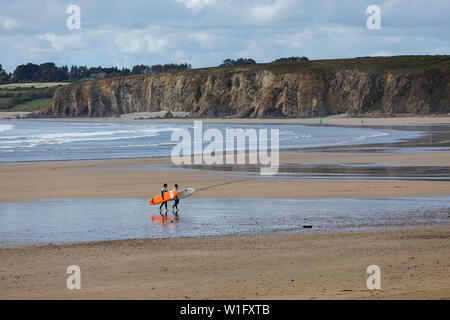 People carrying surfboards walking on sandy beach in Brittany, France Stock Photo