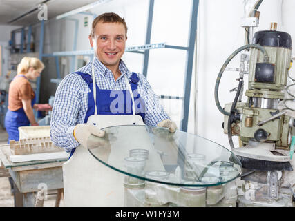 Confident male glazier with female assistant working on curved glass beveling machine in workroom Stock Photo