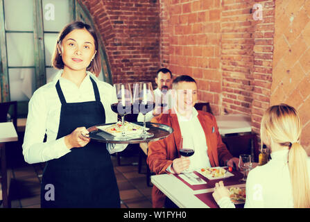 Happy female waiter showing country restaurant to visitors Stock Photo