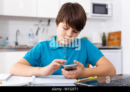 Portrait of boy doing homework and using mobile phone in kitchen at home Stock Photo