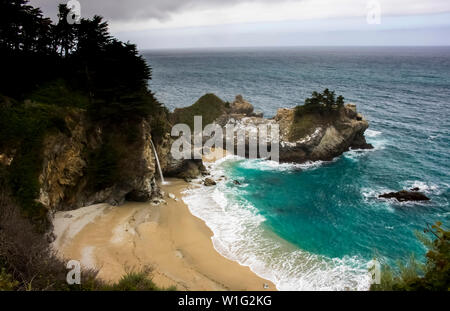 Waterfall pours onto beach from cliffside on California coast along Highway 1 near Big Sur. Stock Photo