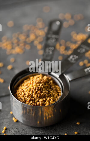 Dried, raw fenugreek seed in measuring scoop on dark moody black kitchen table background with selective focus Stock Photo