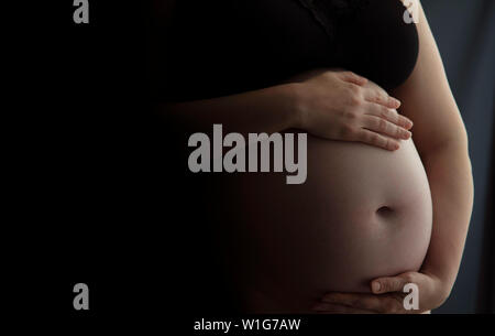 Pregnant woman holding a baby bump against a dark background Stock Photo