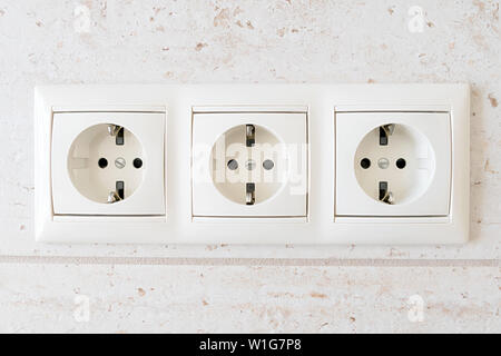 White triple electrical outlet on the textured wall. Stock Photo